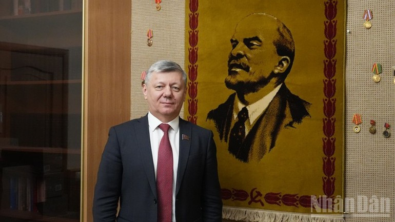 德米特里·诺维科夫同志在俄罗斯联邦共产党莫斯科总部内，站在世界无产阶级领袖弗拉基米尔·伊里奇·列宁的画像旁。