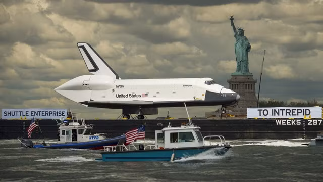 2012年6月6日，在美国纽约86号码头，“企业号”航天飞机在运往“无畏号”航空母舰的途中行经自由女神像。 (Photo: 图：法新社)