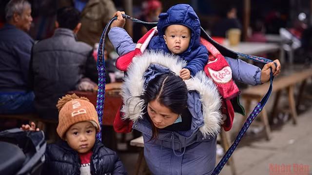 赫蒙族年轻母亲系上皮带，像鸟翼一样保护孩子的瞬间。（成达 摄）