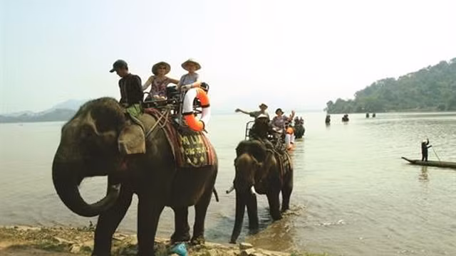 游客骑着大象参观游览大山、村庄和湖水的景色。