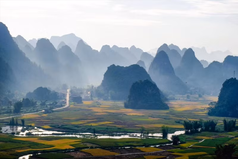 玉昆乡晨曦中若隐若现的石灰岩山脉间，交错着金黄色的稻田。