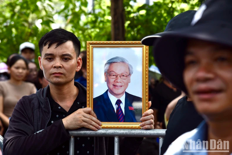 民众手捧阮富仲总书记的遗像等待灵车。