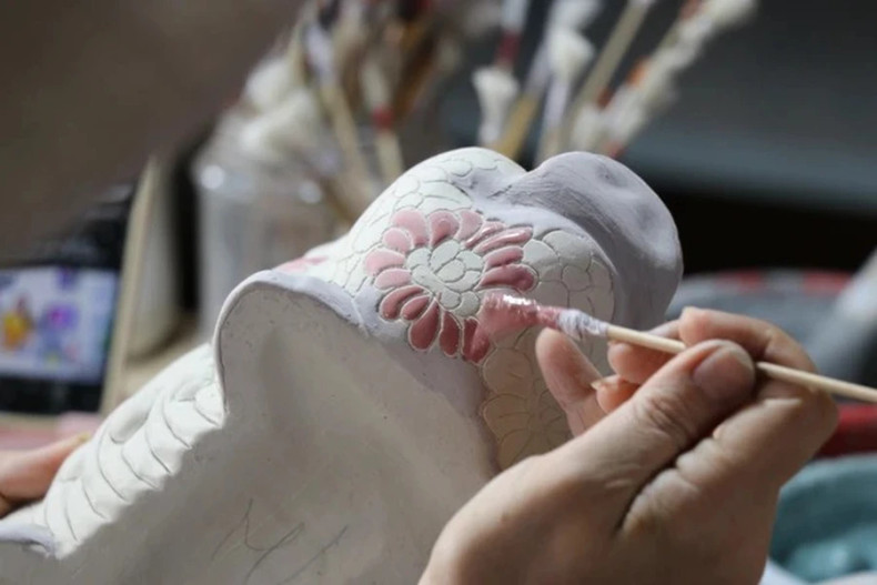 峰山陶瓷作坊的工匠们为陶瓷产品上釉并彩绘装饰。