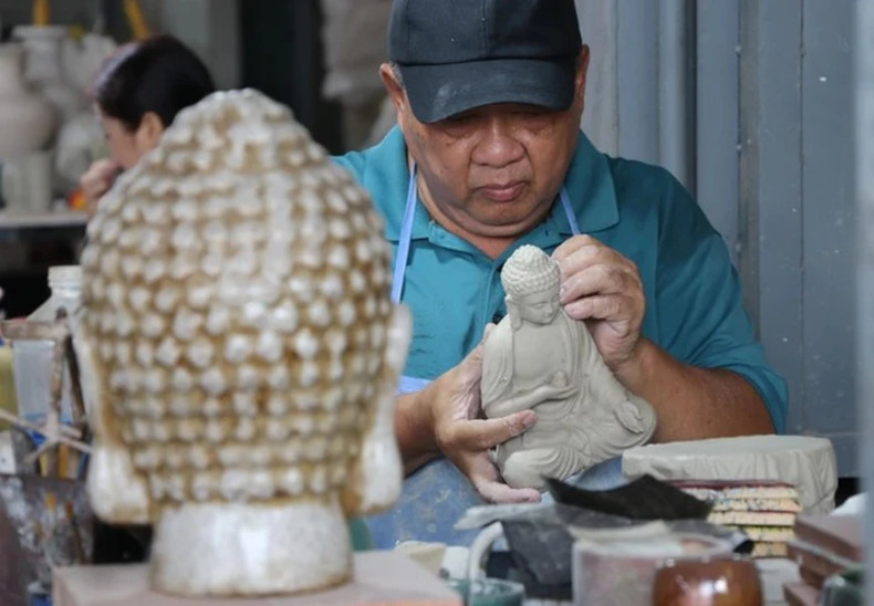 与陶器制作业结伴30年的黎青赝艺人正在制作一尊陶瓷佛像。