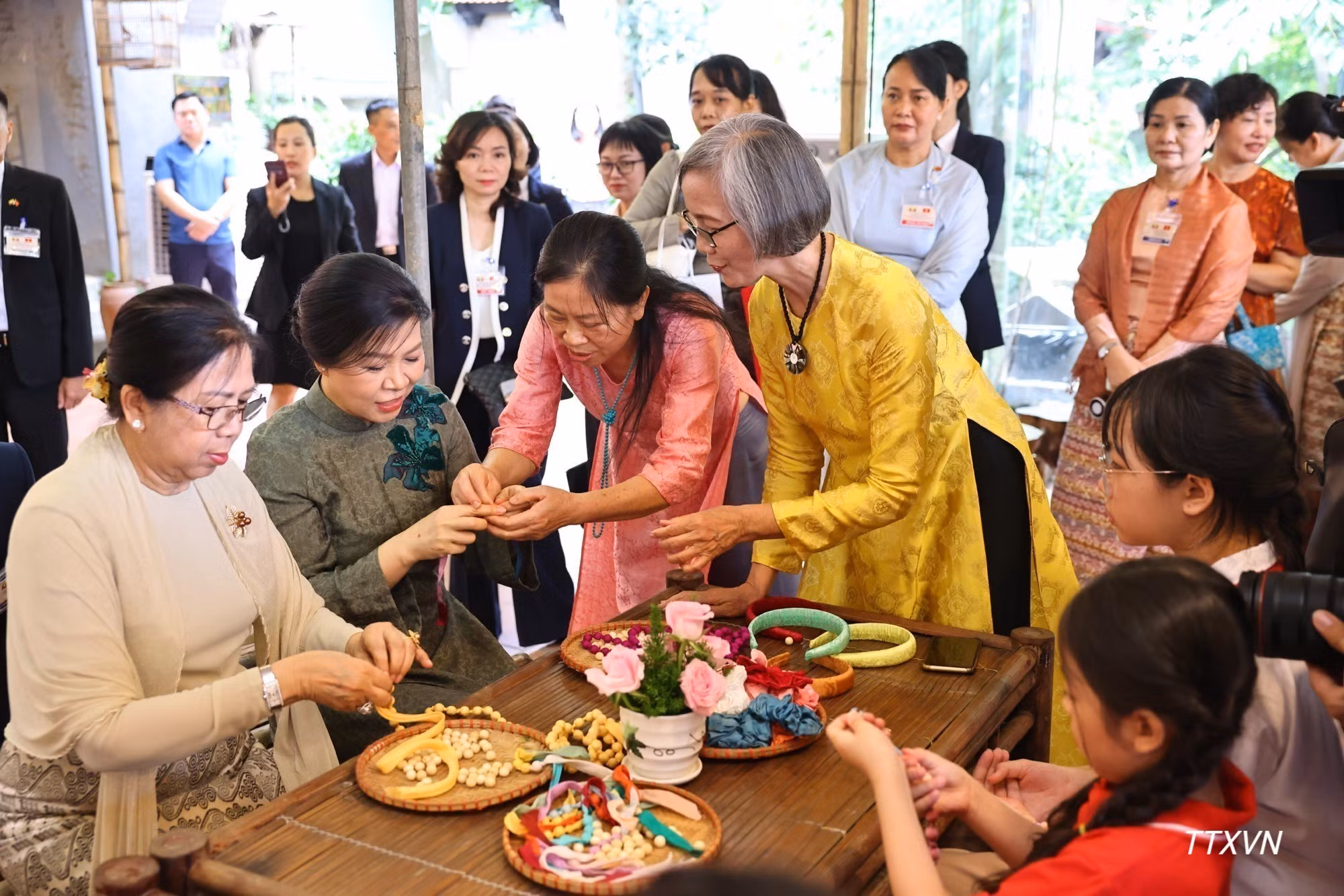 越共中央总书记、国家主席苏林夫人吴芳璃与缅甸总统敏昂莱夫人杜久久拉与当地丝绸世家的青年们一同体验手工串制丝绸珠串。